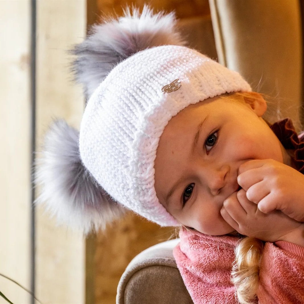 A toddler in a white double pom-pom hat with her mum wearing the Frankie Childrens Bobble Hat in White