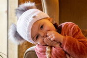 A toddler in a white double pom-pom hat with her mum wearing the Frankie Childrens Bobble Hat in White