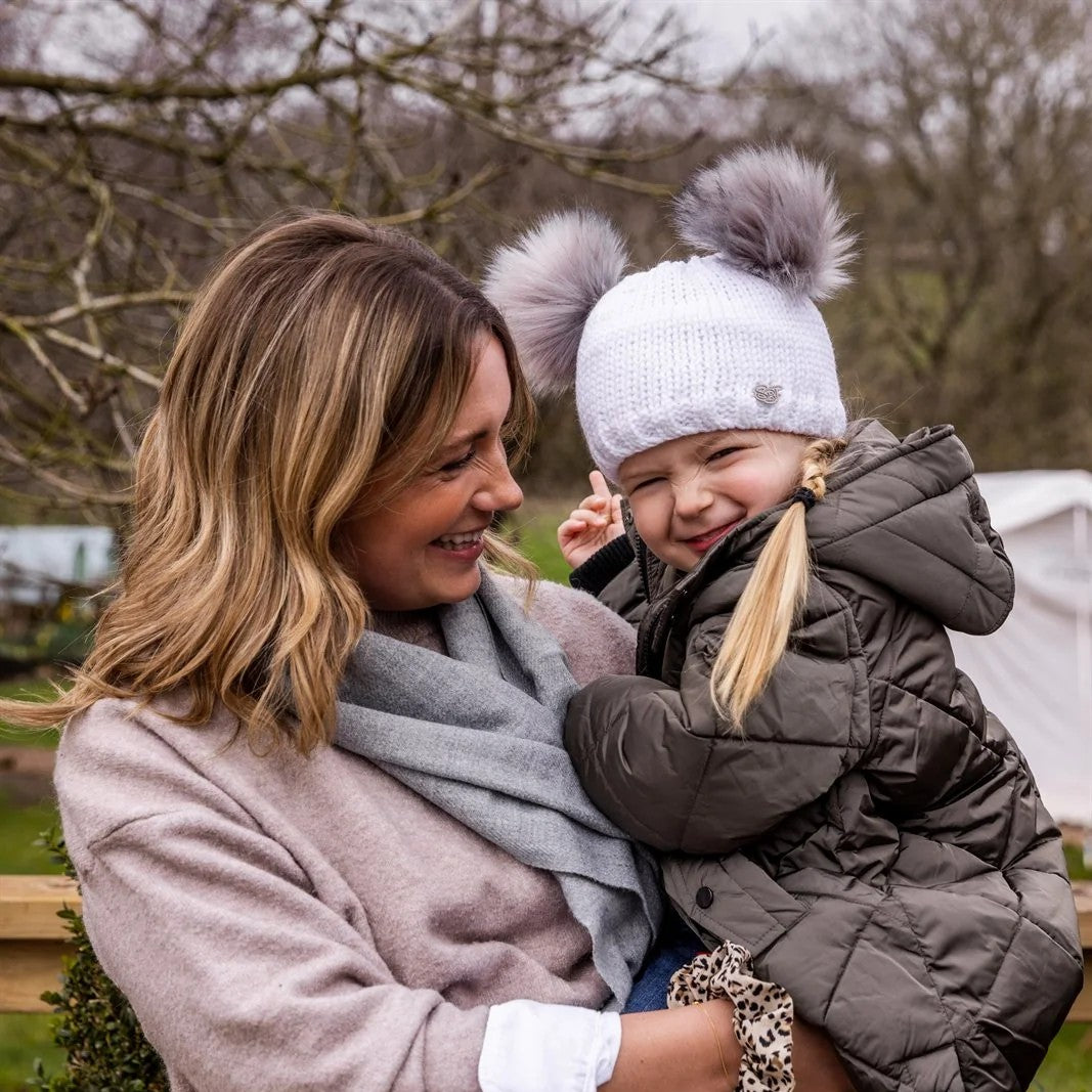 A mum laughing with her toddler outdoors wearing the Frankie Childrens Bobble Hat in White