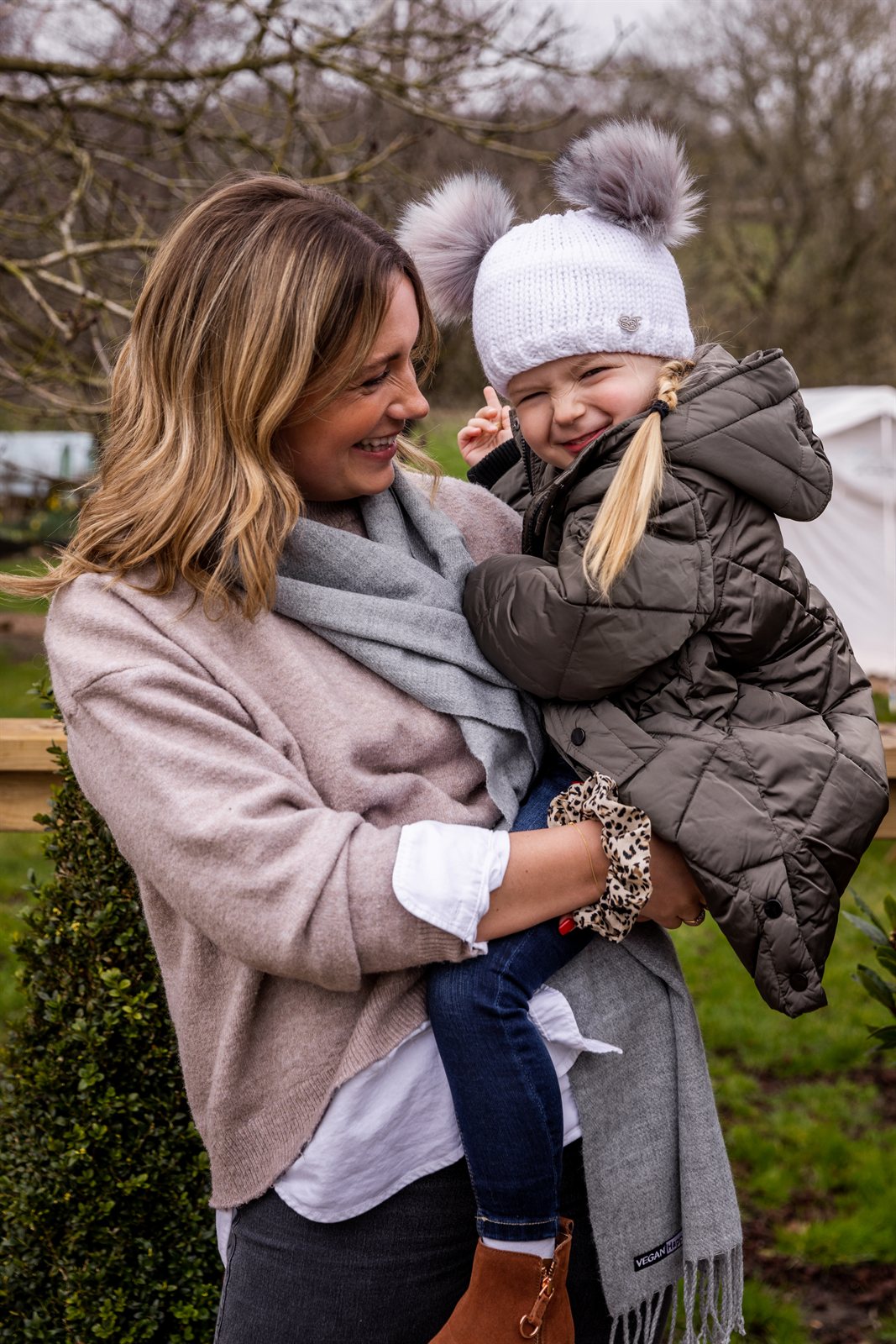 A mum laughing with her toddler outdoors wearing the Frankie Childrens Bobble Hat in White