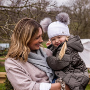 A mum laughing with her toddler outdoors wearing the Frankie Childrens Bobble Hat in White
