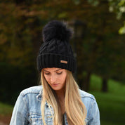 Woman in a denim jacket wearing the SABBOT Linda cable knit bobble hat in black