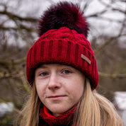 A teenager in tartan in a winter orchard wearing the Linda Bobble Hat and Linda Snood in Burgundy