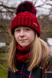 A teenager in tartan in a winter orchard wearing the Linda Bobble Hat and Linda Snood in Burgundy