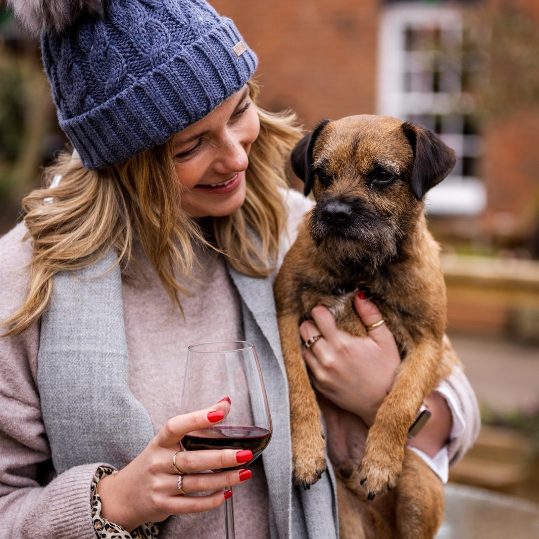 A woman holding a border terrier wearing the Linda Bobble Hat in Denim Blue