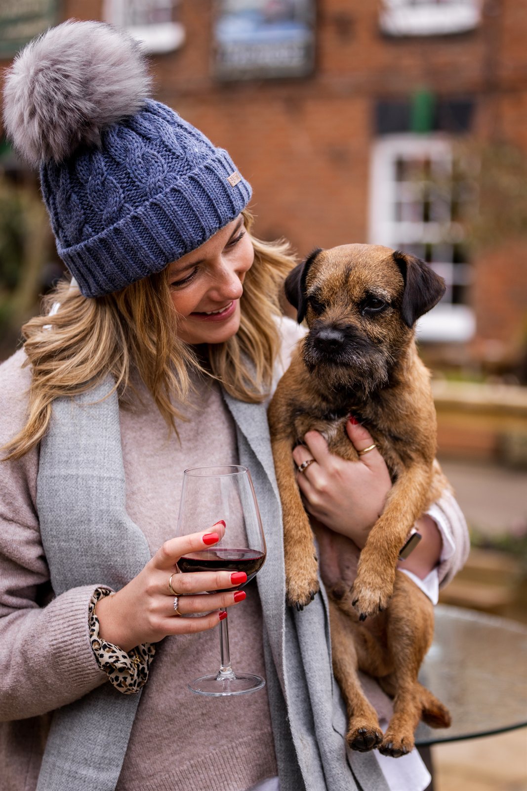 A woman holding a border terrier wearing the Linda Bobble Hat in Denim Blue