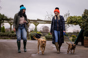 Three friends out walking their dogs wearing the Linda Neon Bobble Hats in Neon Blue and Neon Orange