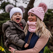 A mum laughing with her toddler outdoors wearing the Linda Bobble Hat and Snood in Pink with a Frankie Childrens Bobble Hat in White