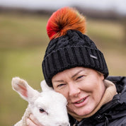 Women cuddling lambs in a field wearing Linda Rainbow Bobble Hat in Black
