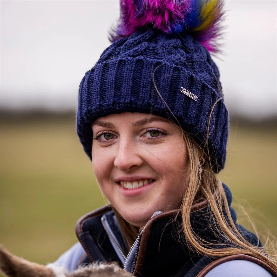 Women cuddling lambs in a field wearing Linda Rainbow Bobble Hat in Navy Blue