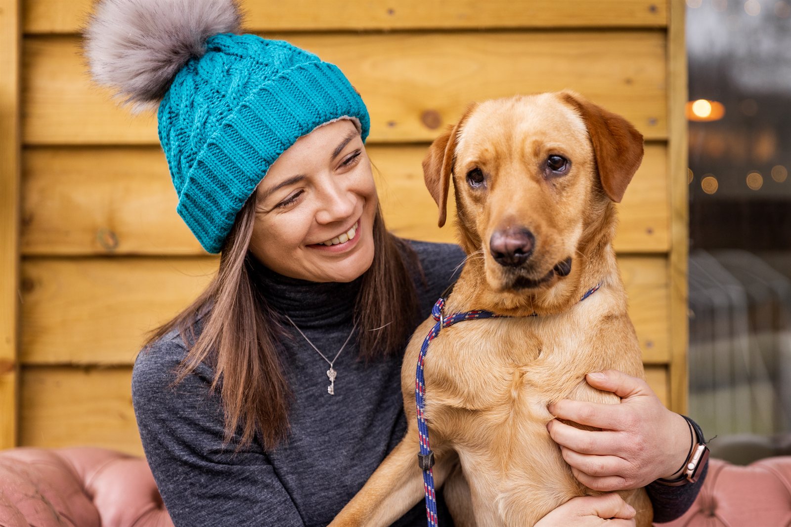 Two women with a labrador on a cabin porch wearing the Linda Bobble Hat in Teal