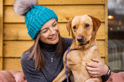Two women with a labrador on a cabin porch wearing the Linda Bobble Hat in Teal