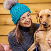 Two women with a labrador on a cabin porch wearing the Linda Bobble Hat in Teal