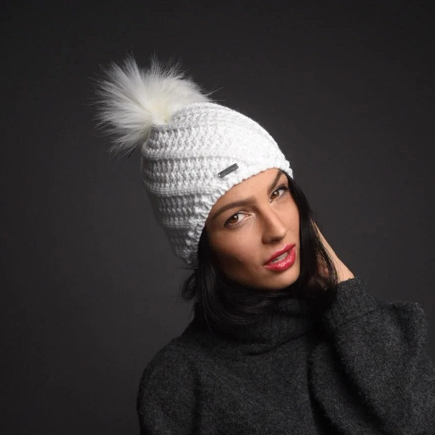 A woman in a grey knit jumper wearing the SABBOT Marta Bobble Hat in White