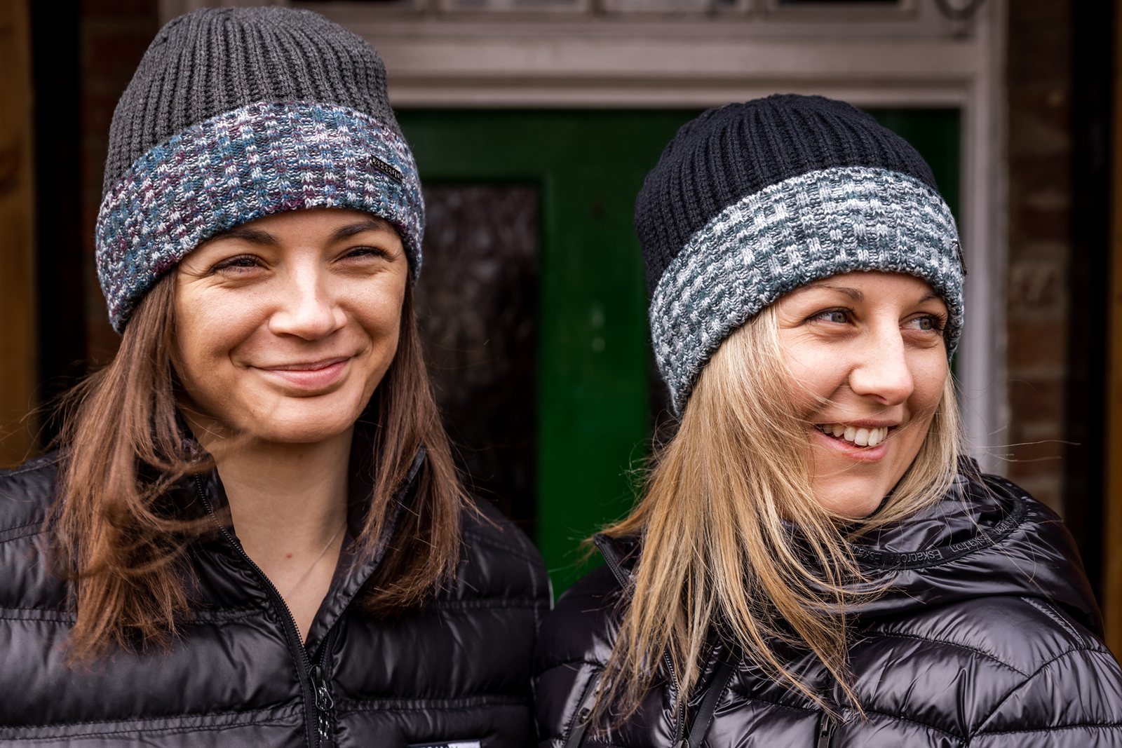 Two women by a red phone box wearing the Morgan Beanies in Black Camo and Grey Camo