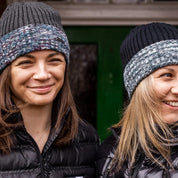 Two women by a red phone box wearing the Morgan Beanies in Black Camo and Grey Camo