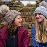 Mum and daughter laughing on stone steps wearing the Petra Fold Bobble Hat in Beige and Light Grey