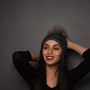 A smiling woman wearing the SABBOT Radka shimmer knit bobble hat with faux fur pom pom