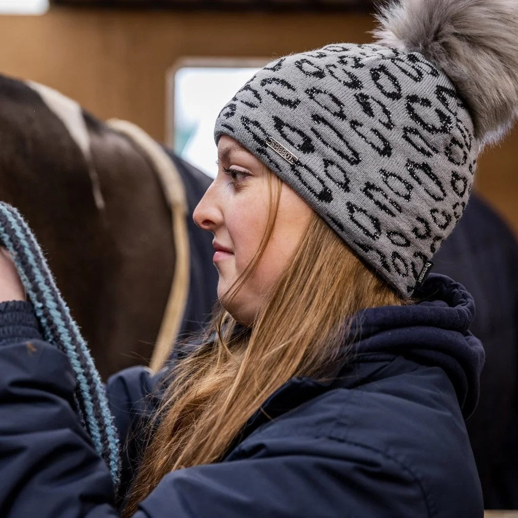 Friends with mugs in a tack room and stables wearing the Saskia Bobble Hat in Grey/Black