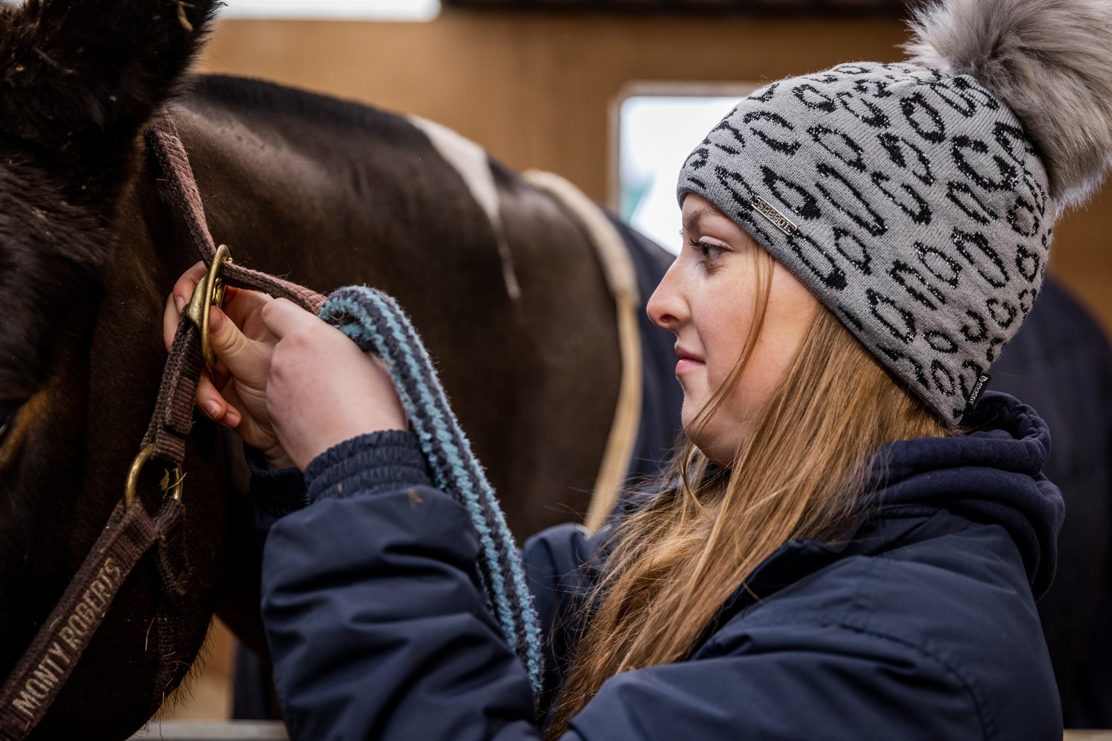 Friends with mugs in a tack room and stables wearing the Saskia Bobble Hat in Grey/Black