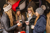 Friends with mugs in a tack room and stables wearing the Saskia Bobble Hat and Headband in leopard print