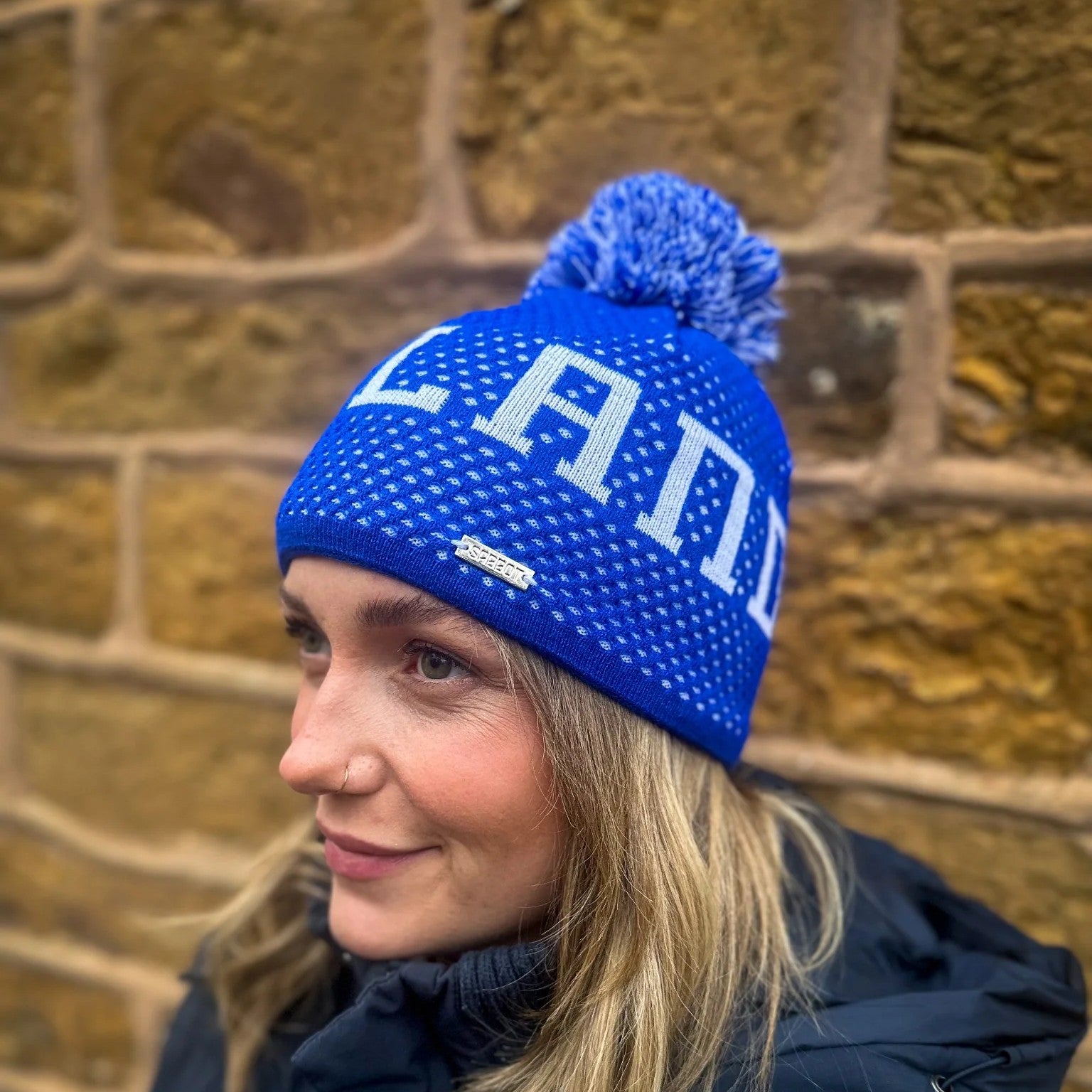 A woman outdoors wearing the SABBOT Scotland Bobble Hat in royal blue with SCOTLAND lettering