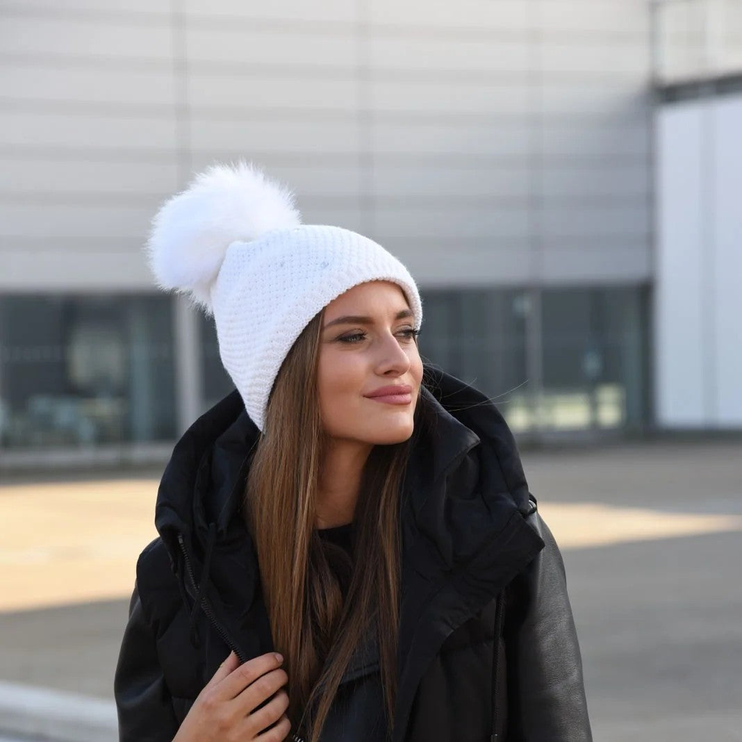 Woman in a black puffer coat wearing the SABBOT Sigrid bobble hat in white with faux fur pom pom