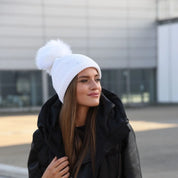 Woman in a black puffer coat wearing the SABBOT Sigrid bobble hat in white with faux fur pom pom