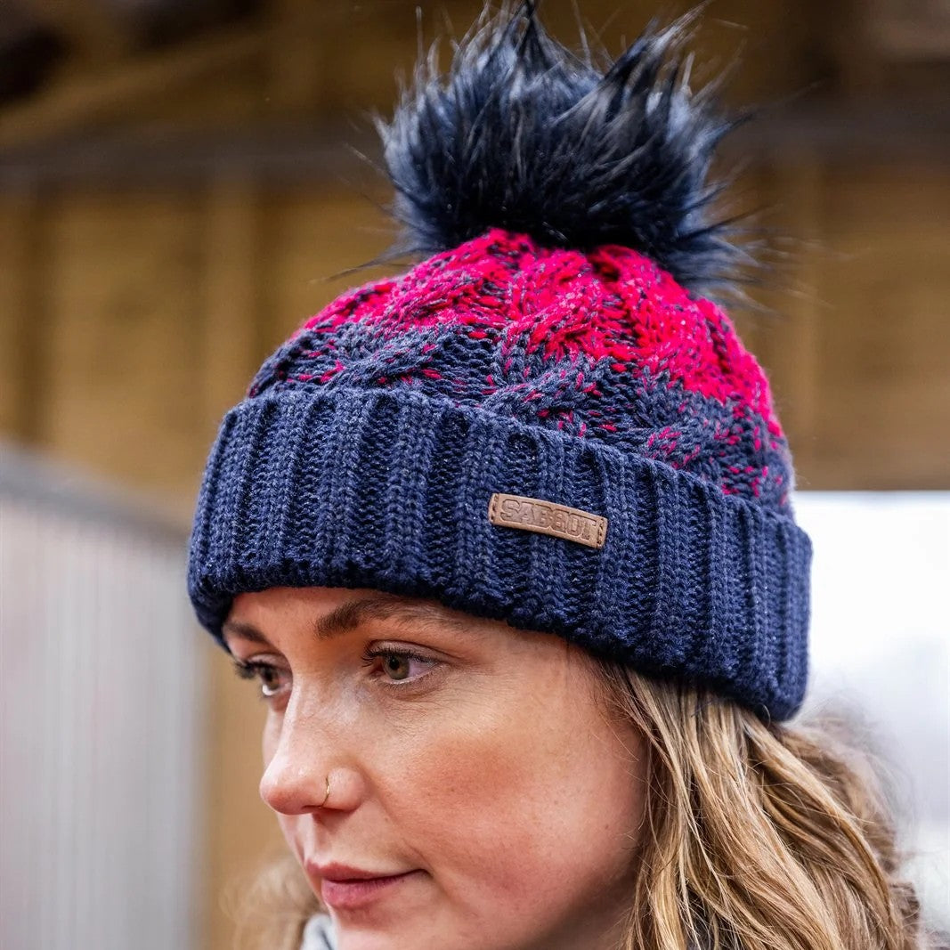 A woman in a navy and red chunky two-tone knit wearing the SABBOT Zuzana Bobble Hat
