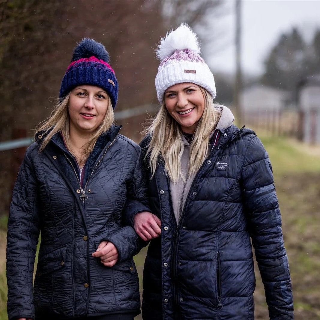 Friends walking arm in arm along a yard track wearing the Zuzana Bobble Hats in Navy/Red and White/Pink