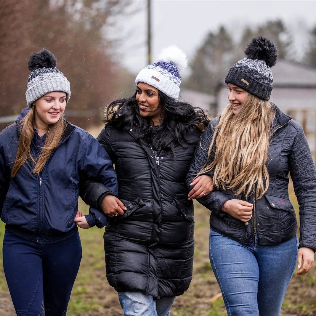 Friends walking arm in arm along a yard track wearing the Zuzana Bobble Hats