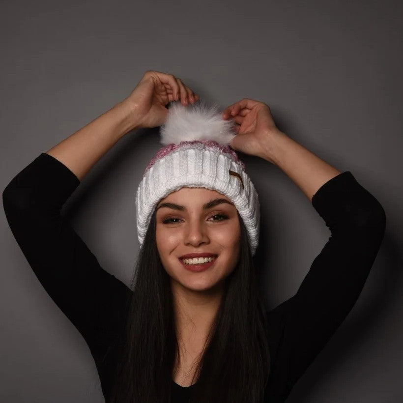 A woman holding the faux fur pom pom of her SABBOT Zuzana Bobble Hat in White/Pink