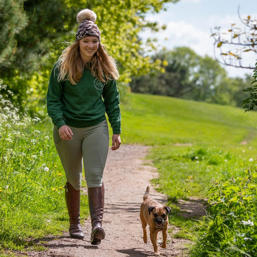 Woman walking her dog on a country path wearing a camo SABBOT Calli bobble hat with faux fur pom-pom