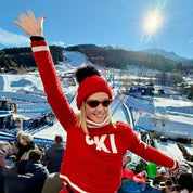 Skier waving on a sunny mountain slope in a neon red SABBOT Eva Krazi bobble hat with black faux fur pom-pom